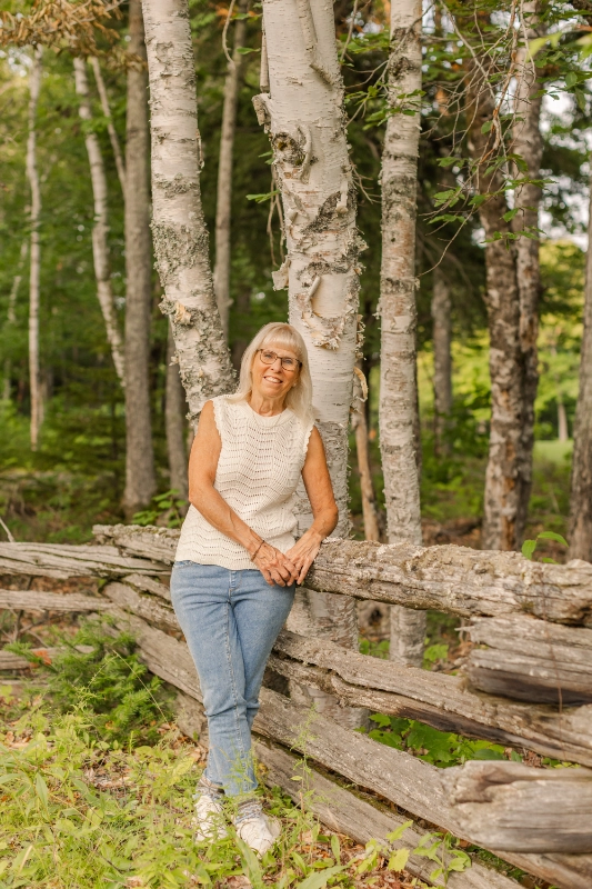 Isabelle Dulac leaning against a split-rail fence among birch trees