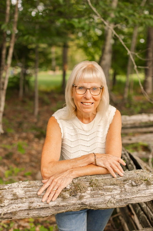 Isabelle Dulac resting on a weathered fence rail in the woods